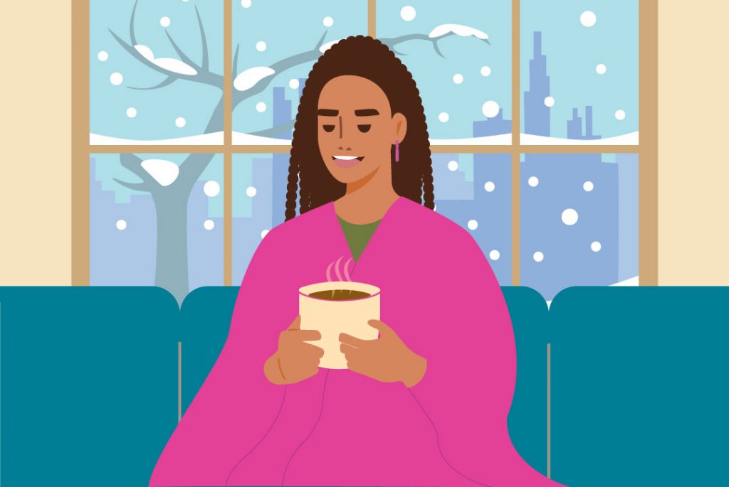 person wearing a blanket enjoying a hot beverage inside on a wintry day